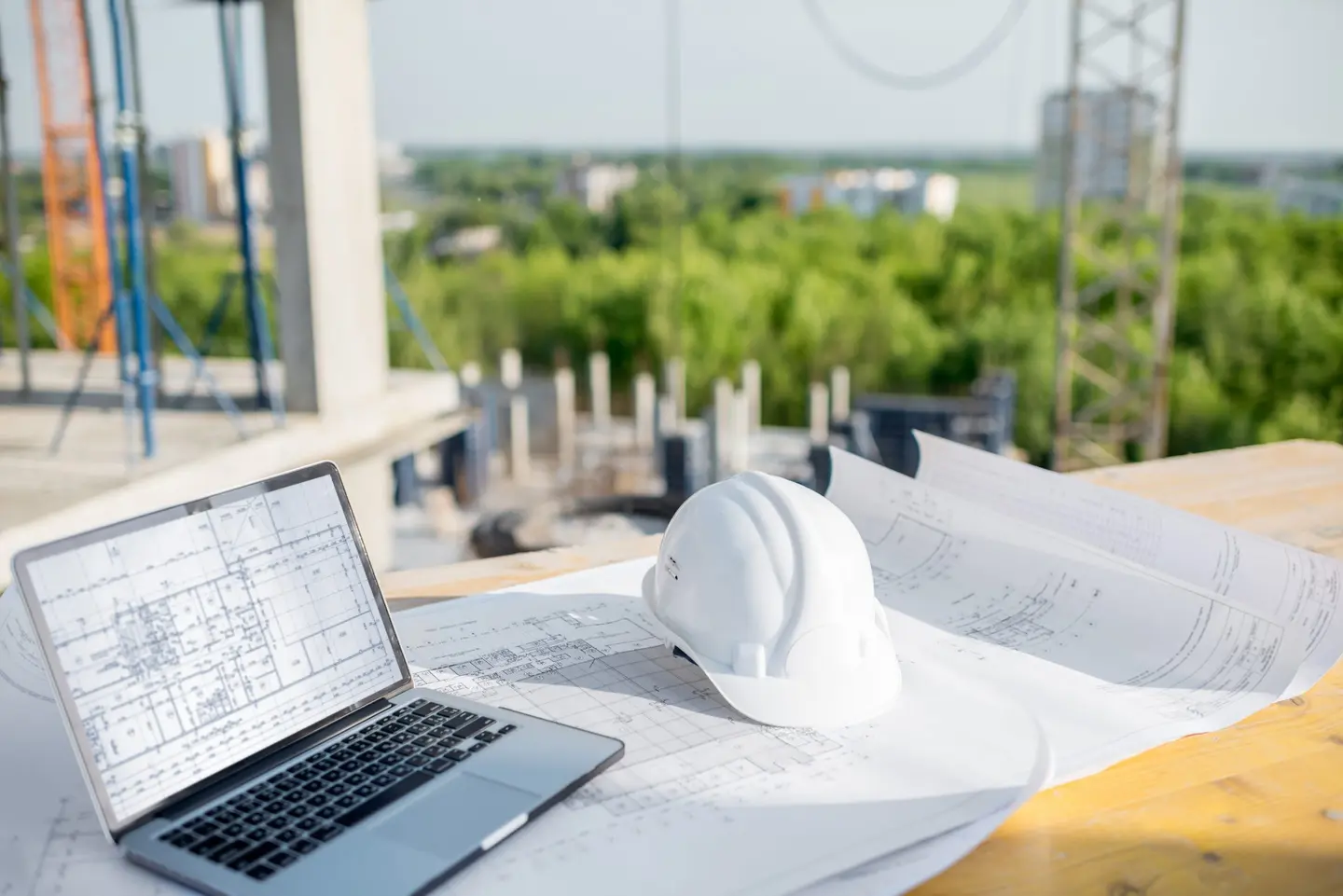 Ordinateur portable, plans et casque de chantier posés sur un chantier en cours