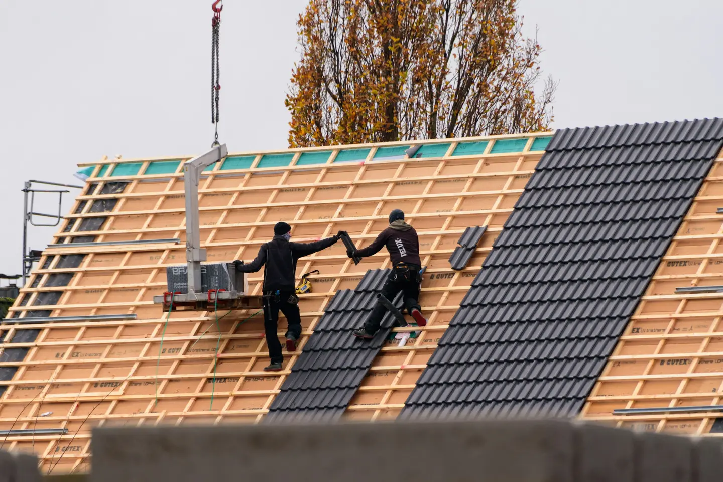 Deux couvreurs posant des tuiles sur une toiture neuve, liteaux et écran sous toiture encore visibles