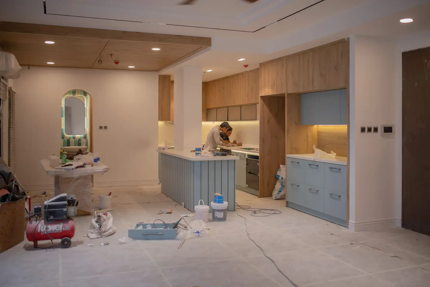 Cuisine en cours de pose : îlot, meubles en bois clair et bleu gris, un ouvrier au travail près du plan de travail