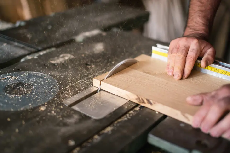 Menuisier découpant une planche de bois sur une scie à table