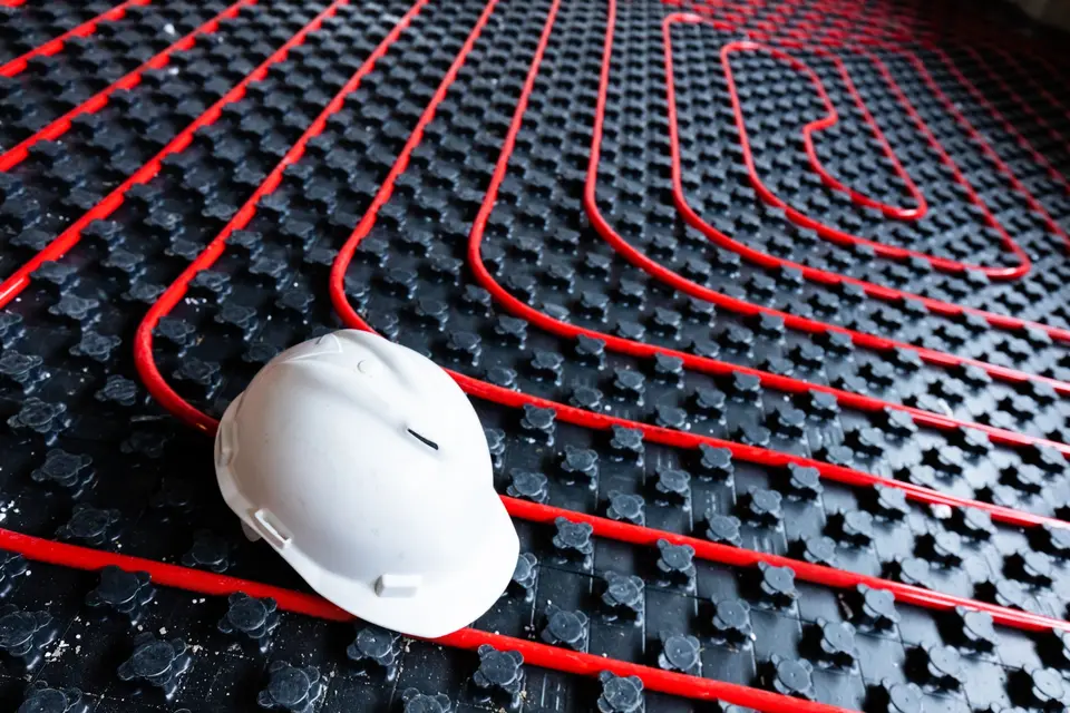 Tubes rouges de plancher chauffant posés sur leurs plaques, un casque de chantier au premier plan
