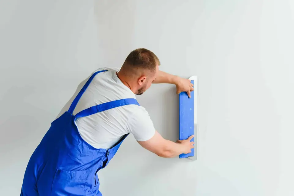 Plâtrier lissant un mur blanc avec une taloche