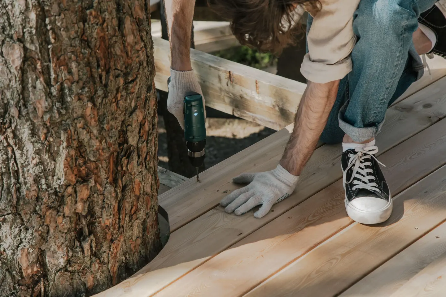 Poseur vissant les lames d’une terrasse en bois découpée autour d’un tronc d’arbre