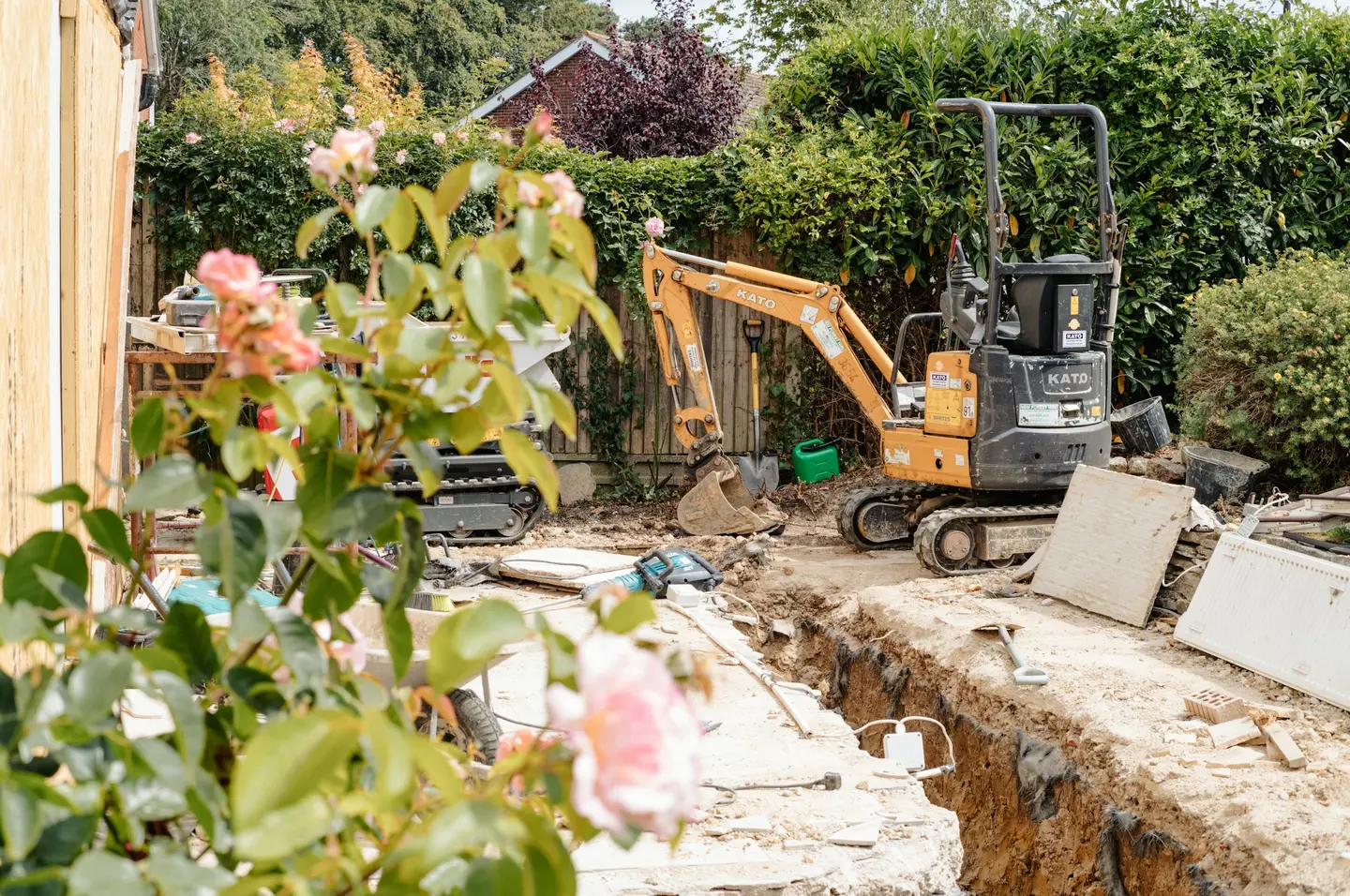 Mini-pelle dans un jardin, à côté d’une tranchée ouverte le long d’une clôture