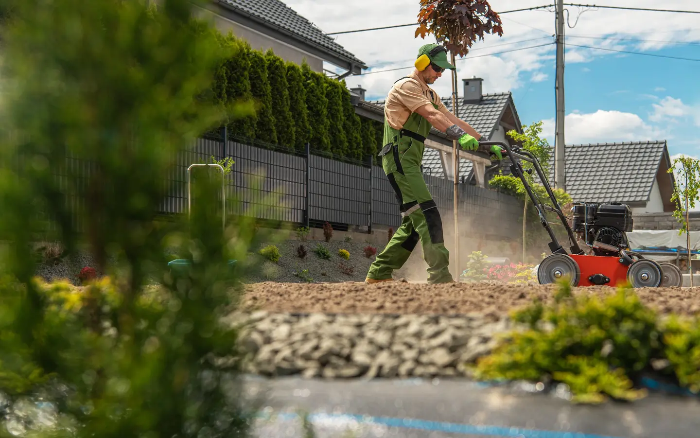 Paysagiste préparant la terre d'un jardin avec une machine à moteur, le long d'une clôture et d'une haie