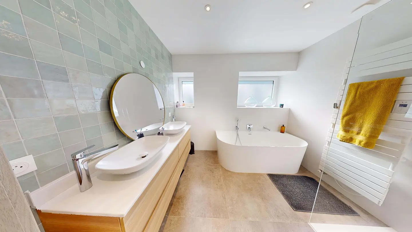 Salle de bain rénovée à Plappeville : double vasque sur meuble en bois, baignoire îlot et carrelage vert d'eau