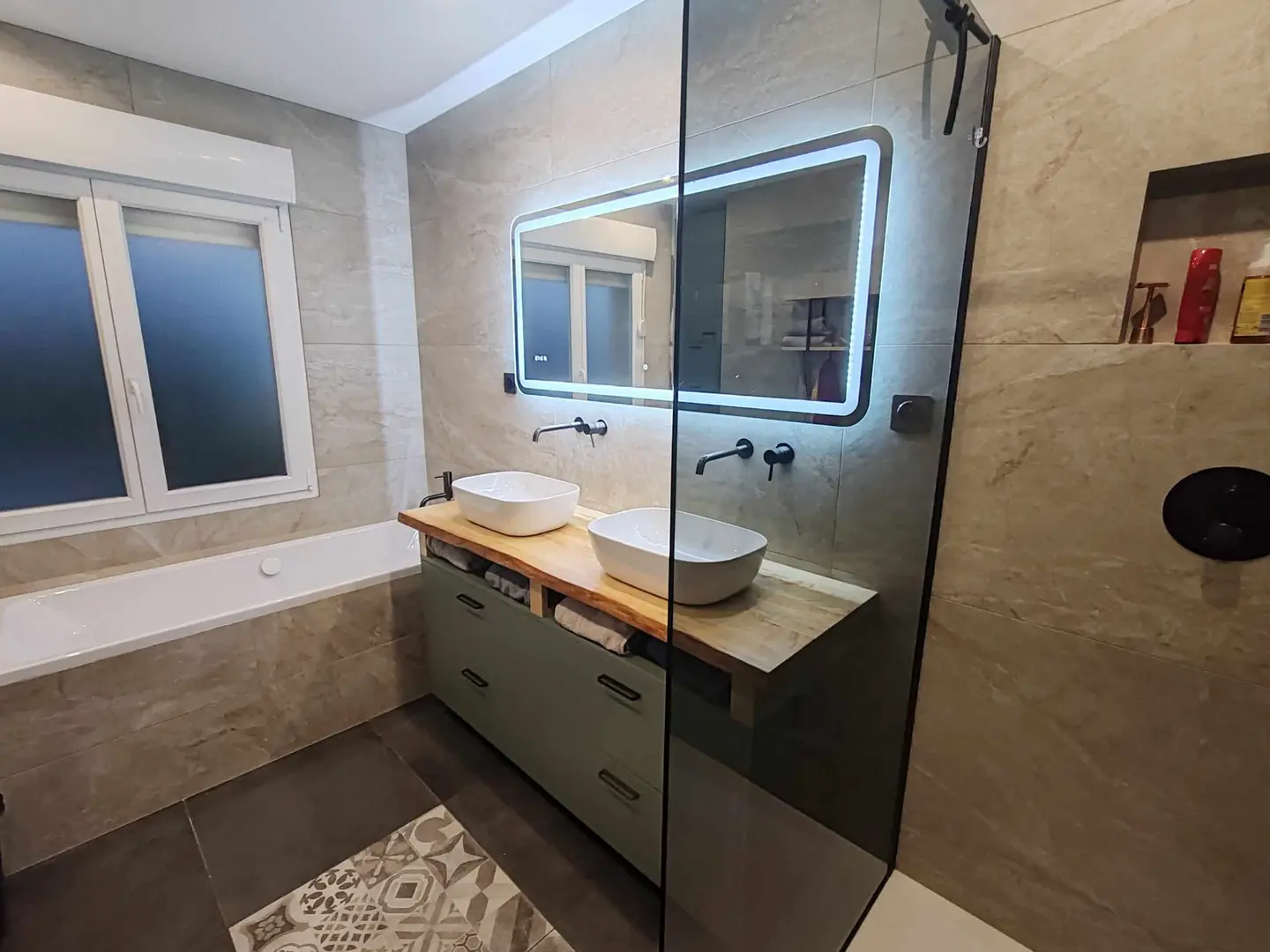 Salle de bain rénovée : douche vitrée, double vasque sur plan en bois, meuble vert sauge, miroir lumineux et baignoire