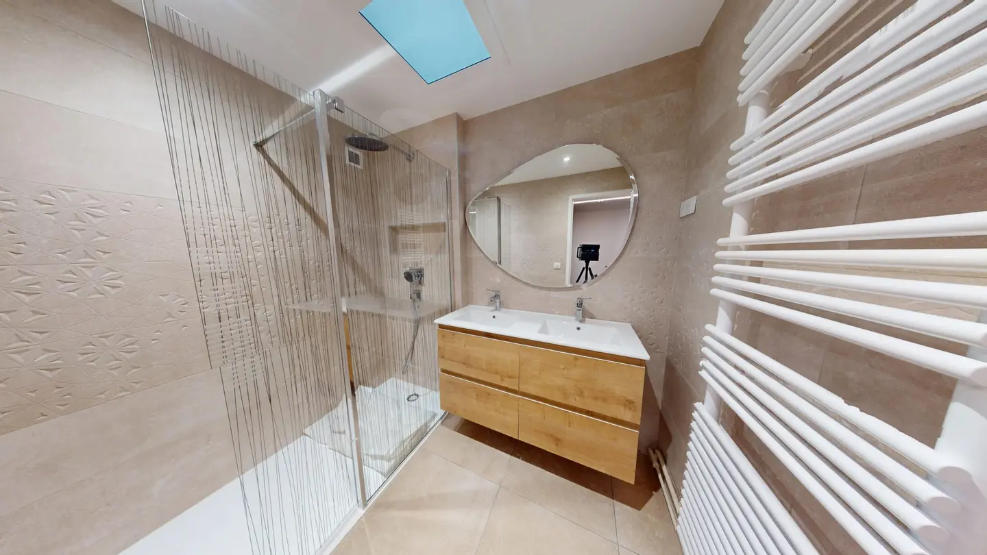 Salle de bain rénovée : douche à l'italienne, meuble vasque en bois, miroir rond et sèche-serviettes