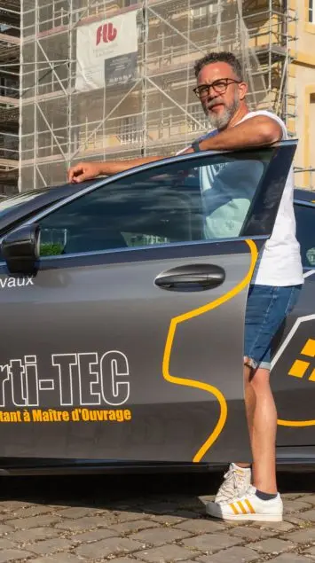 Sébastien Milone devant un échafaudage de chantier, à côté de la voiture arti-TEC